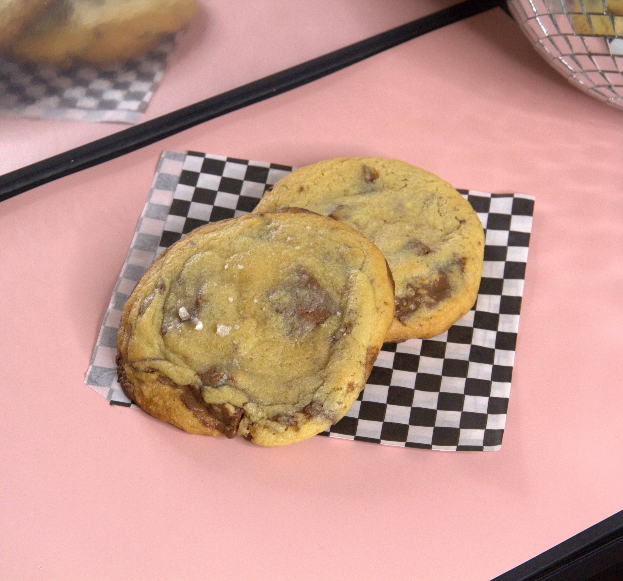 Two big NYC-style chocolate chip cookies on black and white checkered paper