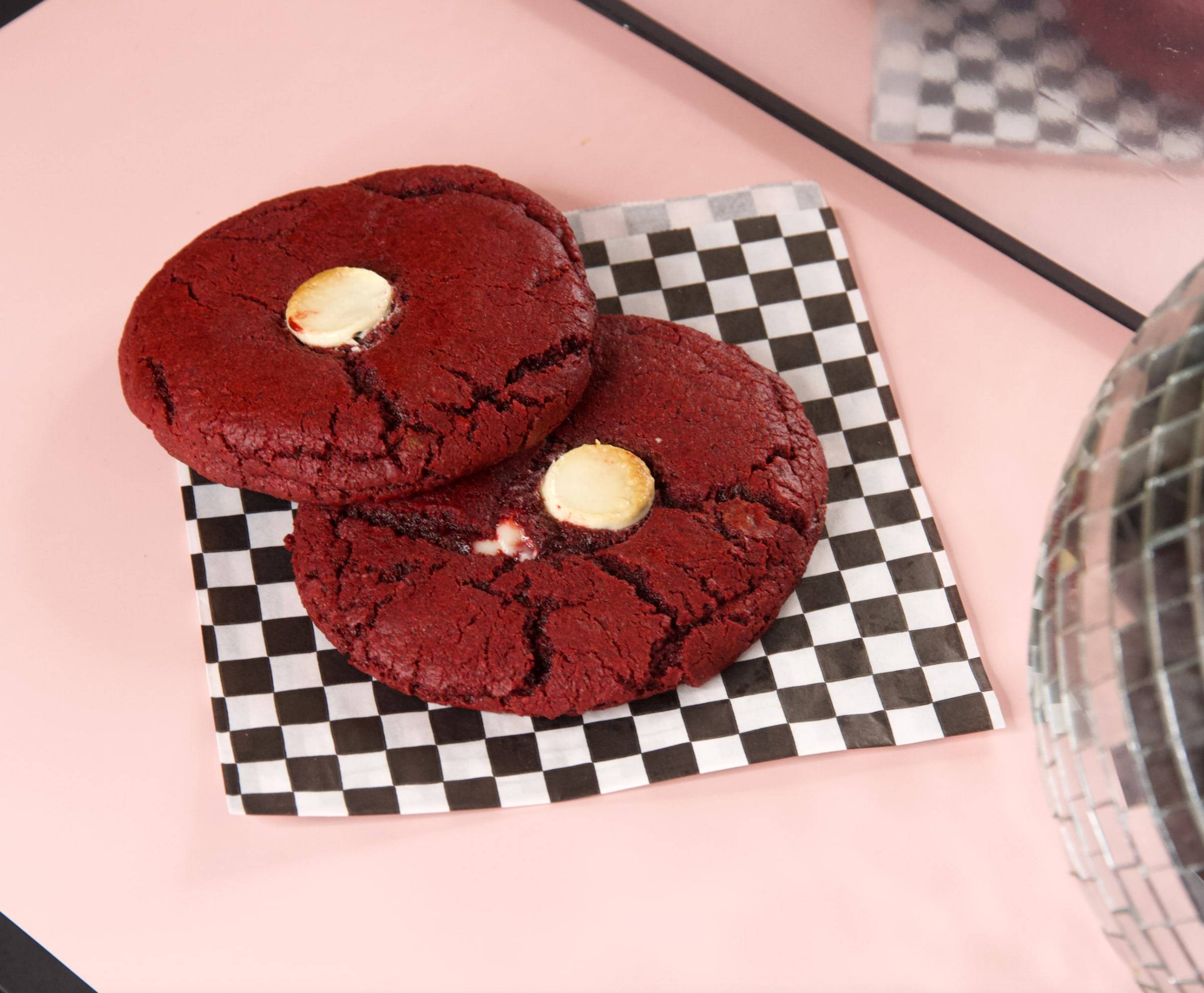 Two deep red velvet NYC cookies with white chocolate on checkered paper