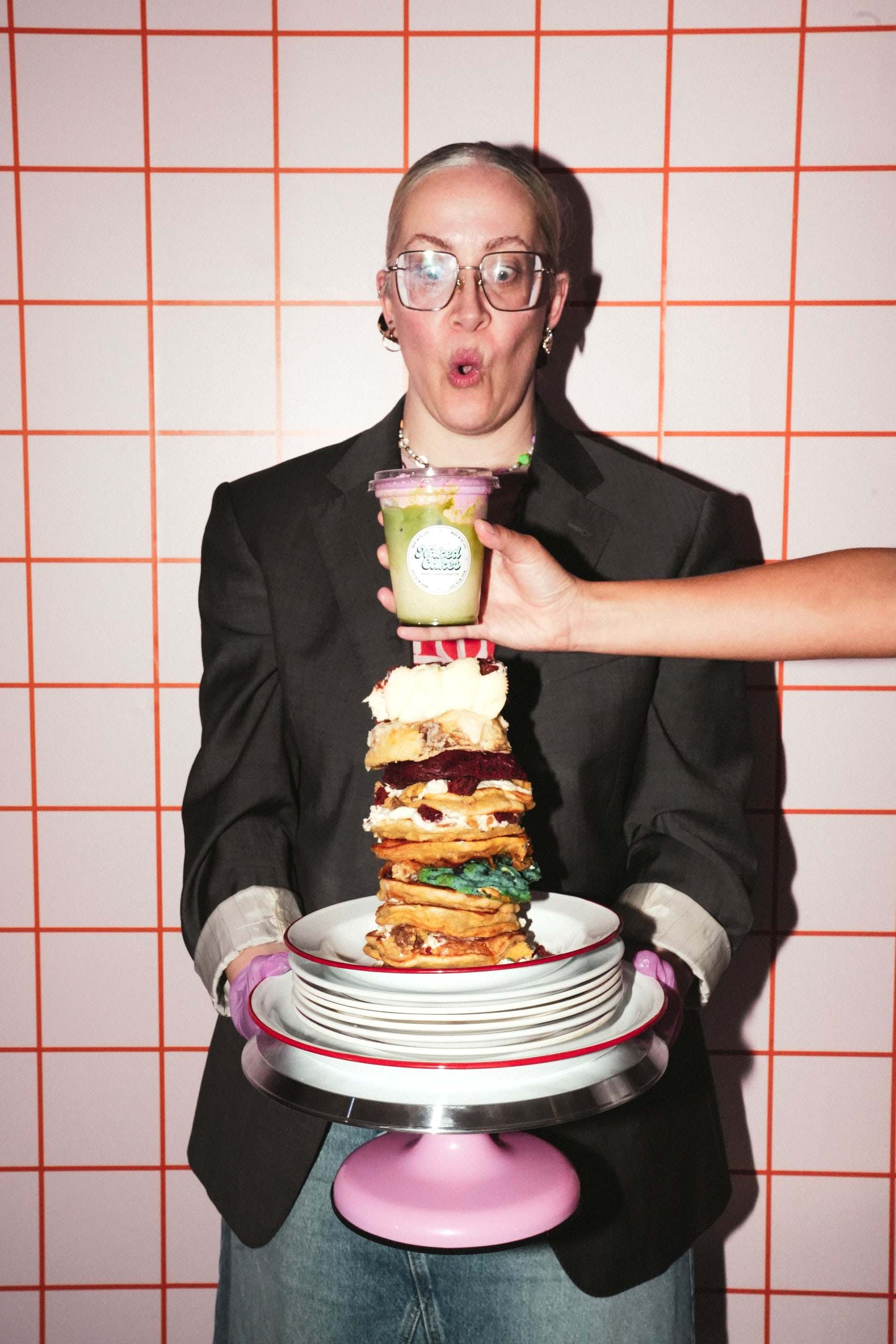 Jessie looking surprised behind a towering stack of cookies with a pink matcha on top