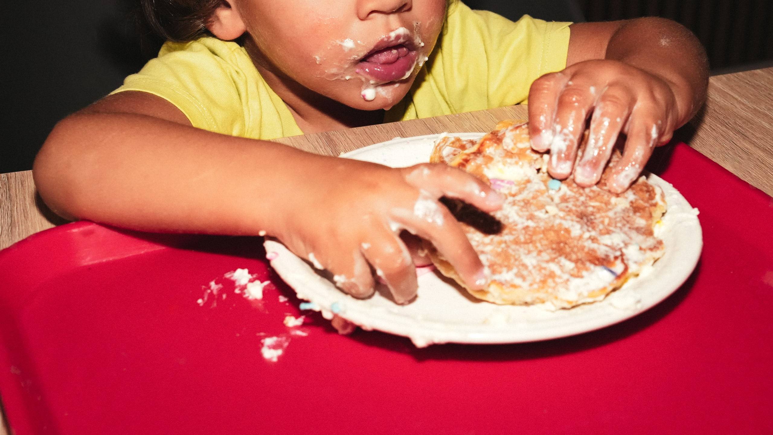 A toddler happily digging into a pancake with both hands