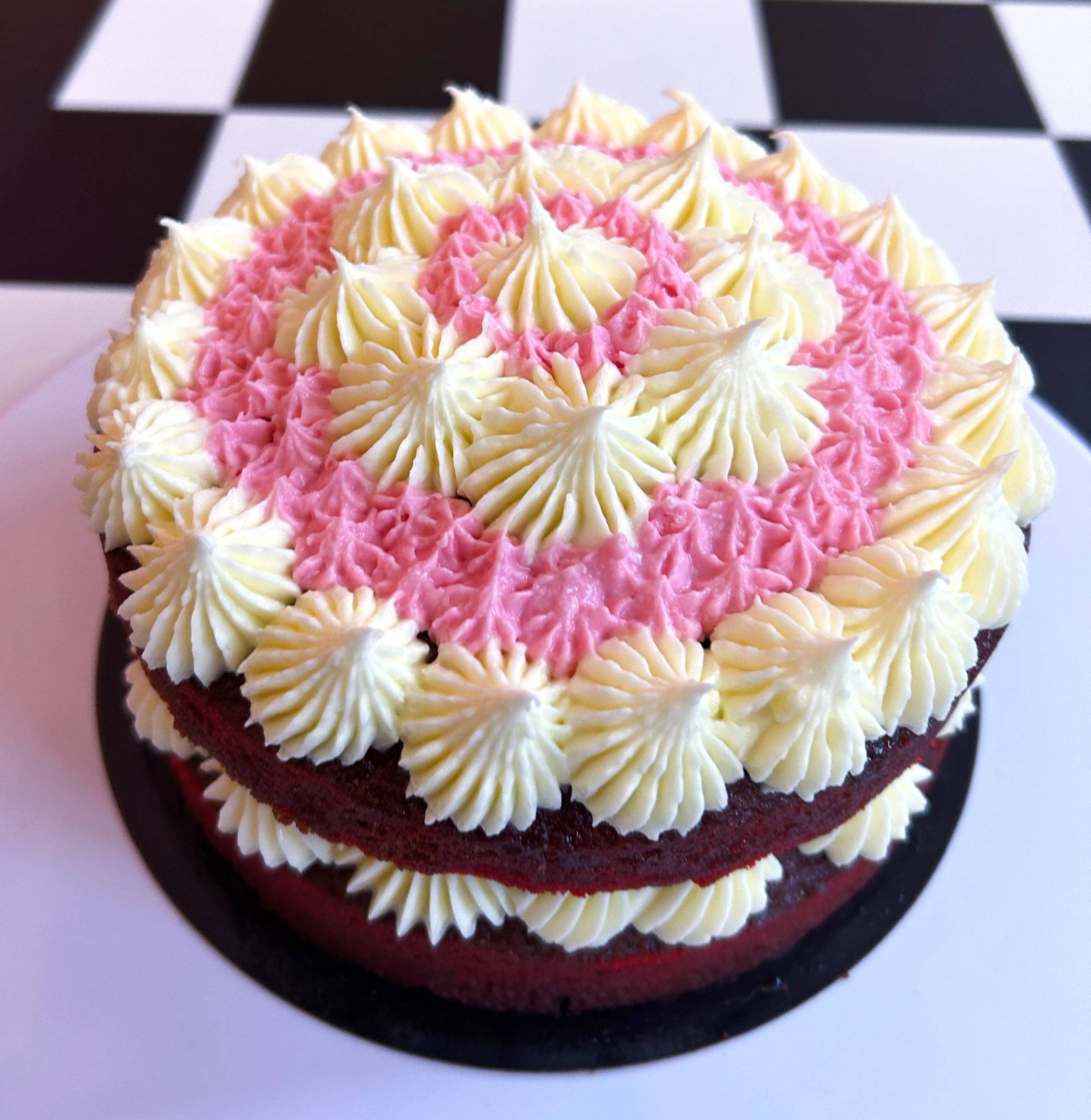 Two-layer red velvet cake topped with white and pink piped frosting rosettes